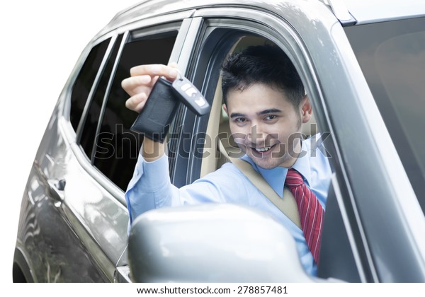Portrait of happy worker showing a car key\
inside the car, isolated on white\
background