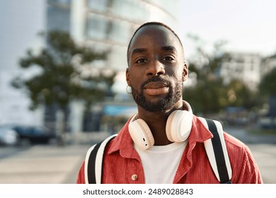 Portrait of happy young adult African man hipster standing on city street outdoors looking at camera. Smiling cool generation z Black hipster guy wearing red shirt headphones posing for close up photo - Powered by Shutterstock