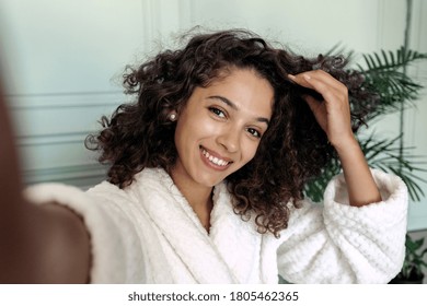 Portrait of happy young adult afro american woman in bathrobe taking self photo on camera, spending weekend at home, sitting in living room, making online stream for beauty blog - Powered by Shutterstock