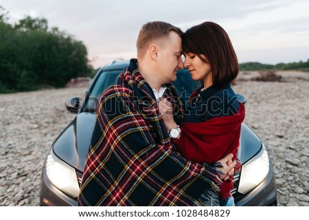 Portrait of happy young adult couple on roadtrip. Man embrace woman near car.