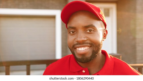 Portrait of happy young African American smiled man in red T-shirt and hat standing outside the house on summer day. Close up of male cheerful courier in uniform. Deliveryman with smile at street. - Shutterstock ID 1806290440