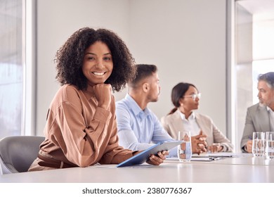 Portrait of happy young African American business woman at diverse team office meeting. Smiling confident professional businesswoman company employee leader with tablet sitting in board room. - Powered by Shutterstock