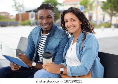 portrait of happy young african college couple sitting on bench