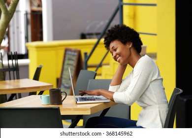 Portrait Of A Happy Young African Woman Relaxing In Outdoor Cafe And Using A Laptop