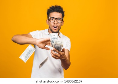 Portrait of a happy young afro american man throwing out money banknotes isolated over yellow background.