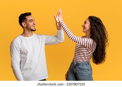 Portrait Of Happy Young Arab Couple Giving High Five To Each Other, Cheerful Middle Eastern Man And Woman Enjoying Teamwork, Celebrating Common Success While Standing Over Yellow Studio Background - Shutterstock ID 2207807255