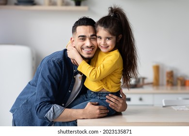 Portrait Of Happy Young Arab Dad And Little Daughter Posing Together In Kitchen Interior, Cute Small Girl Embracing Her Middle Eastern Father And Smiling At Camera, Daddy And Kid Having Fun At Home