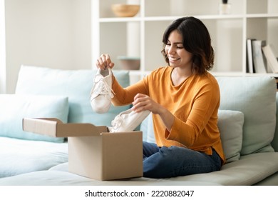 Portrait Of Happy Young Arab Woman Unboxing Parcel With Shoes At Home, Smiling Middle Eastern Female Opening Cardboard Box And Looking At New Pair Of White Sneakers, Satisfied With Online Shopping