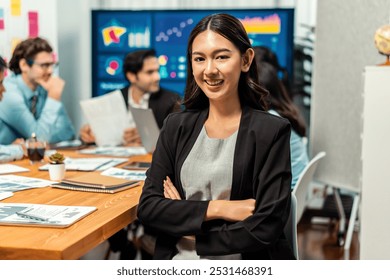 Portrait of happy young asian businesswoman or analyst looking at camera with her colleague analyzing data analysis in dynamic business strategy investment planning meeting. Habiliment - Powered by Shutterstock