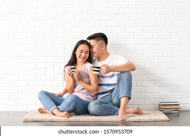 Portrait of happy young Asian couple drinking coffee near white brick wall