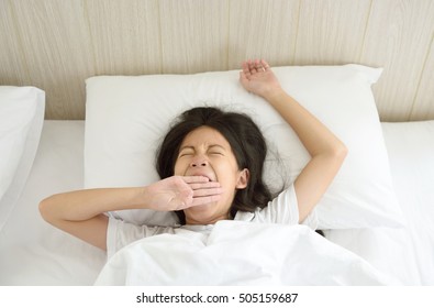 Portrait des glücklichen jungen asiatischen Mädchens mit langen schwarzen Haaren, die morgens im Bett gähneln