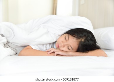 Portrait Of Happy Young Asian Girl With Long Black Hair Sleeping Comfortably On The Bed In Bedroom At Home. Cheerful Kid Model Lying On The Tummy.