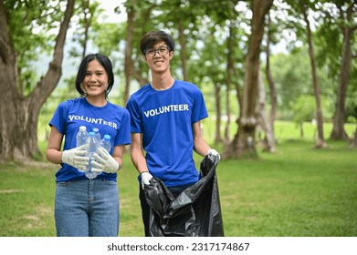 A portrait of happy young Asian male and female volunteers with plastic bottles and a plastic garbage bag standing in the public park. Volunteer work, Charity, Ecology