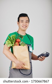 Portrait Of Happy Young Asian Supermarket Worker With Paper Package And Payment Terminal