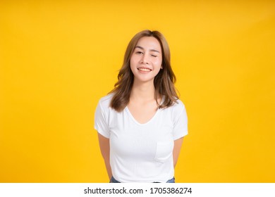 Portrait Happy Young Asian Woman Laughing Blink, Wink Eye Joyful Funny Positive Emotion In White T-shirt, Yellow Background Isolated Studio Shot And Copy Space.