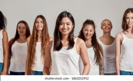 Portrait of happy young asian woman in white shirt smiling at camera. Group of diverse women posing, standing isolated over grey background. Diversity concept. Front view. Selective focus