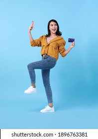 Portrait Of A Happy Young Asian Woman Celebrating With Mobile Phone And Credit Card Isolated Over Blue Background.