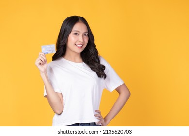 Portrait Of A Happy Young Asian Woman Wearing White Shirt Holding Bank Card, Credit Card Isolated On Yellow Background. Business Online Shopping Concept.