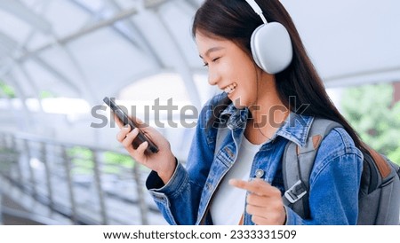 Portrait of happy young asian woman listening music online with wireless headphones from a smartphone in the city