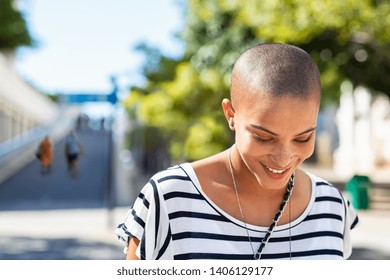 Portrait of happy and young bald woman smiling. Carefree trendy girl with bald head after cancer chemotherapy treatment. Stylish and beautiful woman feeling free in a city street. - Shutterstock ID 1406129177