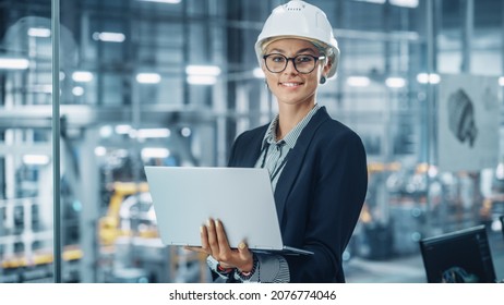 Portrait of a Happy Young Beautiful Female Engineer Wearing White Hard Hat, Using Laptop Computer in Office at Car Assembly Plant. Industrial Specialist Working on Vehicle Design in Modern Facility. - Shutterstock ID 2076774046