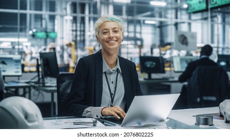 Portrait of a Happy Young Beautiful Female Engineer Sitting at a Desk, Using Laptop Computer in Office at Car Assembly Plant. Industrial Specialist Working on Vehicle Design in Modern Facility. - Shutterstock ID 2076802225