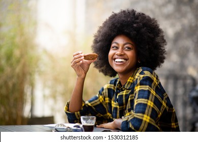 Portrait of happy young black woman eating cookie