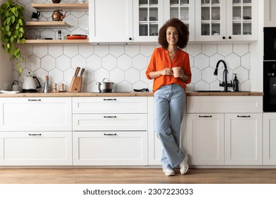 Portrait Of Happy Young Black Woman With Cup Of Coffee Posing In Cozy Kitchen Interior At Home, Cheerful African American Female Enjoying Caffeine Drink And Smiling At Camera, Relaxing At Home - Powered by Shutterstock