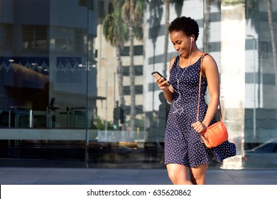 Portrait Of Happy Young Black Woman Looking At Mobile Phone And Listening To Music