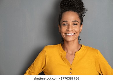 Portrait of happy young brazilian woman standing on gray wall and looking at camera. Smiling african american girl isolated against grey background with copy space. Mixed race woman with curly hair. - Shutterstock ID 1770389966