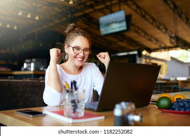 Portrait of happy young business woman celebrating success with arms up in front of laptop. Mixed race female won a lot of money in lottery prize, raised arms with fists. Freelancer finished project.