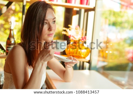 Portrait of happy young business woman with mug in hands drinking coffee at restaurant
