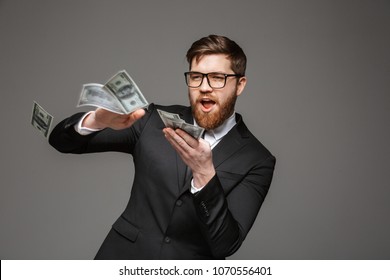 Portrait of a happy young businessman throwing out money banknotes isolated over gray background