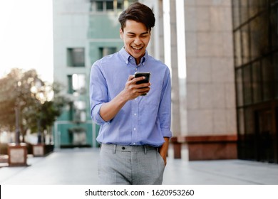 Portrait of a Happy Young Businessman Using Mobile Phone in the Urban City. Lifestyle of Modern People. Front View. Modern Building as background - Powered by Shutterstock