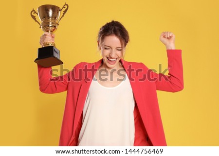 Portrait of happy young businesswoman with gold trophy cup on yellow background