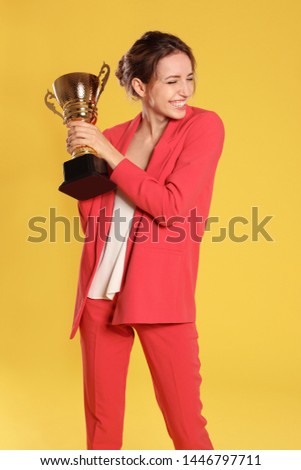 Portrait of happy young businesswoman with gold trophy cup on yellow background