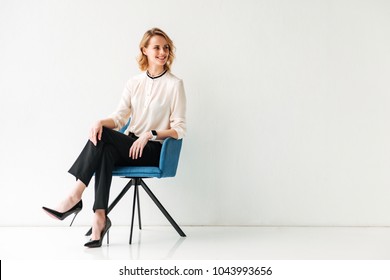 Portrait Of A Happy Young Businesswoman Sitting In A Chair Against White Background And Looking Away At Copy Space