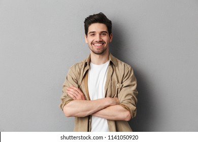 Portrait of a happy young casual man standing with arms folded isolated over gray background