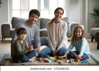 Portrait of happy young Caucasian family with little children sit on warm floor in living room playing toys together, smiling parents have fun engaged in game activity with small preschooler kids