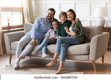 Portrait of happy young Caucasian family with two small kids sit relax on couch in new design living room. Smiling parents renters buyers with little children rest in own renovated home on weekend. - Shutterstock ID 1863887530