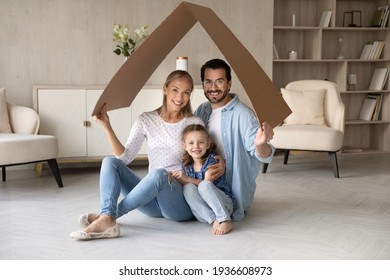 Portrait of happy young Caucasian family with daughter relax under roof celebrate relocation to own home. Smiling parents with girl child enjoy new house or apartment. Rental, real estate concept.