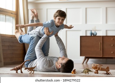 Portrait of happy young Caucasian father lying on floor at home play with cute little 6s son. Loving dad feel playful engaged in funny game activity, hold in hands fly with excited small boy child. - Shutterstock ID 1894279522