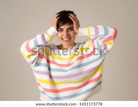 Portrait of happy young caucasian female laughing and hands on head in surprise wearing multicolor striped jumper isolated over neutral background. People, human emotions and celebration.