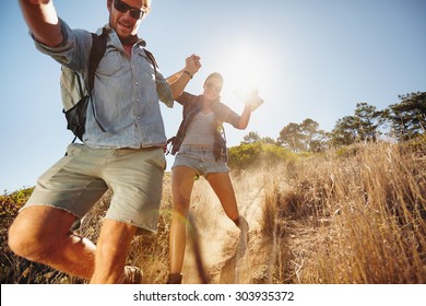 Portrait of happy young couple having fun on their hiking trip, sliding down the mountain trail. Caucasian hiker couple enjoying themselves on summer vacation.