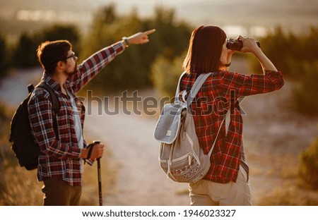 Portrait of happy young couple having fun on their hiking trip. Caucasian and asian hiker couple enjoying themselves on summer vacation. They are watching nature with binoculars.