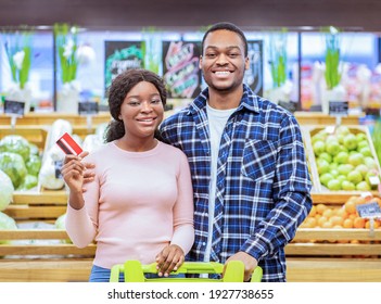 Portrait Of Happy Young Couple Holding Credit Card, Looking At Camera And Smiling At Supermarket. Positive Millennial Family Promoting Contactless Payment While Shopping At Mall