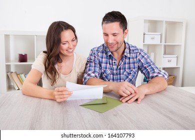 Portrait Of A Happy Young Couple At Home Reading Paper