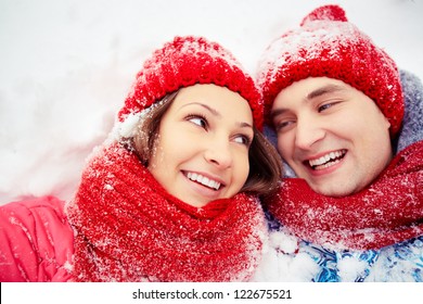 Portrait Of Happy Young Couple Lying On Snow And Looking At One Another