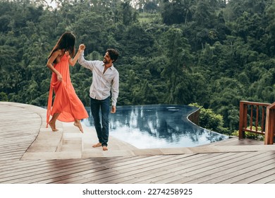 Portrait of happy young couple on vacation having fun near swimming pool. Young man and woman at luxury resort poolside. Man helping woman to walking down the steps. - Powered by Shutterstock