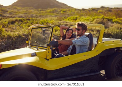 Portrait of happy young couple on a road trip in a beach buggy. Smiling young woman with her boyfriend driving car in countryside.